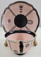 Photo of the cup and saucer showing the front pattern with black circular and linear designs and pink background.