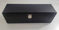 Front view of closed black wooden wine gift box with silver metal clasp, showing overall shape and color.