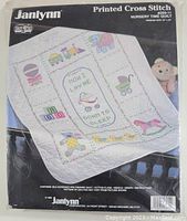 Full front of Janlynn Printed Cross Stitch Nursery Time Quilt kit packaging showing the printed quilt with nursery themed stitch patterns including toys, animals, and text.