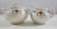 Side view of the sugar bowl and creamer set showing shape, handles, and decorative motifs