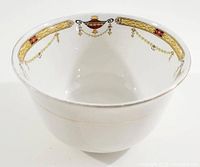 White porcelain sauce bowl with detailed red and gold urn and garland pattern near rim shown from front angle.
