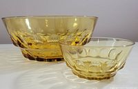 Both large and small Indiana Glass amber Thumbprint pattern bowls shown together on a surface with clear lighting to show color and pattern.