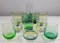 Front view showing all 11 glasses with various green tones, floral decorations, and shapes.