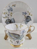 Teacup and saucer with blue and green floral motif, gold trim, cup on wooden stand, front view
