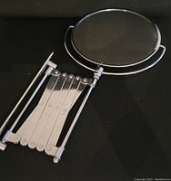 Wall mount round mirror with a polished chrome extendable accordion arm, mirror frame approximately 7 inches in diameter.
