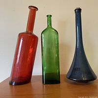 Photo of three tall coloured glass bottles in red, green, and blue showing their shapes and relative sizes.