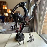 Photo showing one large black glazed pottery deer statue and two small metal wire deer sculptures on a table near a window.