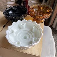 Three Fenton sawtooth hobnail candle holders in white, black, and amber, shown from the top to display candle slots.