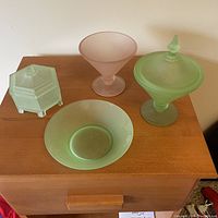 Set of four frosted glass bowls placed on wooden surface. Two of the bowls have lids. Colors visible are green and pink. Shapes include round and hexagonal.