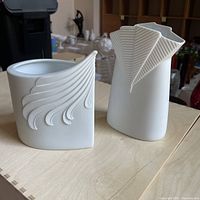 Two white bisque porcelain vases with distinct relief patterns displayed on a table.