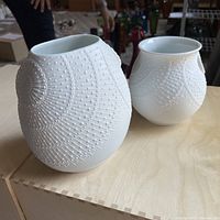 Pair of white bisque vases showing raised dot and circular design pattern, two sizes displayed side by side on wooden surface.