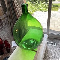 Large green glass bottle shown standing upright on a box near a window showcasing its size and green translucent glass material.