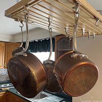 Three copper pots hanging from ceiling rack showing exteriors and patina