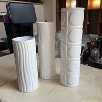 Set of three white ceramic cylindrical vases with different surface textures arranged on a table, showing distinct patterns on each vase.