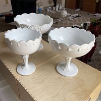 Set of three white glass pedestal bowls arranged on a wooden surface showing their size and rim detail.