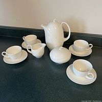 Coffee pot, sugar bowl, creamer and four cups with saucers displayed on countertop