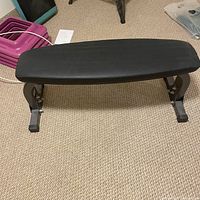 Top view of flat weight bench showing black padded surface and metal legs on carpeted floor.