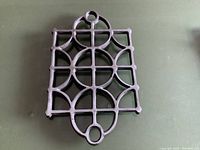 Black iron trivet with geometric and circle pattern on green surface.