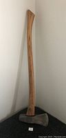 Full view of axe standing against a wall, showing long wooden handle and metal axe head.