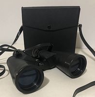 Black hard carrying case with snap button and shoulder strap beside binoculars.