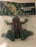Front view of green plastic frog in original packaging with header card showing product name and details