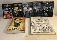Front view of five Harry Potter DVD cases arranged in a row with Harry Potter and the Cursed Child book and a Harry Potter coloring book in front.