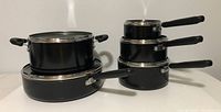 Front and side view of stacked Lagostina cookware showing pans and saucepans with handles and lids.