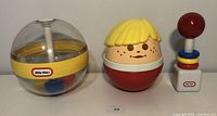 Three vintage Little Tikes toys: Toddle Tot Roly Poly Boy, baby rattle with rings, and Whirlee Ball toy with colored balls inside a dome