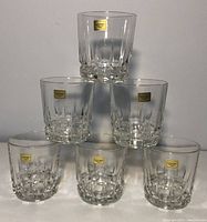 Front view of all six clear Luminarc whiskey/rock glasses stacked in a pyramid, showing original gold Luminarc labels and faceted base design.