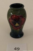 Front angled view showing the raised red pansy design on jade green ceramic body.