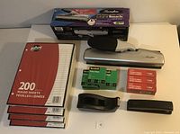 Photo of all items including stapler in box, desk punch, packages of ruled sheets, tape dispenser, and staples.