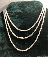 Pearl necklace displayed draped on a green velvet bust showing the length and pearl size.