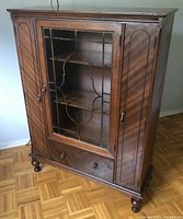 Closed view of solid wood china cabinet showing front glass paneled door with ornate wood grid, two side wooden doors, and bottom drawer.