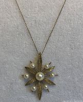 Front view of starburst pendant showing textured gold petals and pearls
