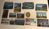 Display of multiple vintage postcards including scenic views of ships, landscapes, and landmarks with both folded and flat style postcards