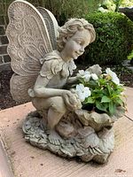 Side-angle view of detailed concrete angel planter with white flowering plant inside.