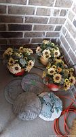 Three ceramic pots filled with faux sunflowers and greenery arranged on a floor corner next to four decorative garden stones with detailed designs and inscriptions