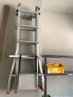 Ladder in upright A-frame configuration leaning against wall with plastic tote on adjacent shelf