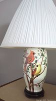 Close-up of pleated white lamp shade and detailed cardinal bird painted on white ceramic base with branches.