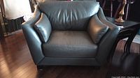 Front view of Laken grey leather wide lounge chair with two small cushions on armrests. Chair stands on four short block legs.