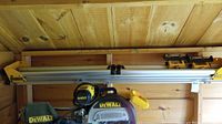Photo showing the full DeWalt DW723 mitre saw stand mounted horizontally on a wooden wall, including rails, support arms, and clamps.
