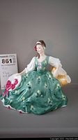 Full view of Royal Doulton figurine Elyse seated with green dress and white hat with pink bow.