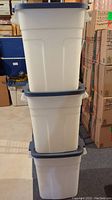 Three stacked white Rubbermaid Roughneck storage totes with blue lids shown from side angle.