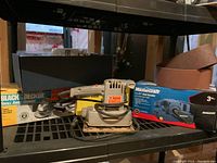 Photo showing Black & Decker small angle grinder box with spare wheels along with other boxes on a plastic shelf.