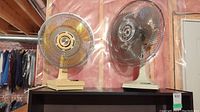Two table oscillating fans placed on shelf, showing size and general condition.
