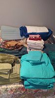 Stack of assorted folded linens including teal towels, fabric pieces, placemats, and towels in different colors