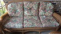 Front view of three-seater wicker couch with floral cushions outdoors