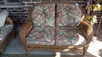 Front view of natural brown wicker loveseat with two back and two seat cushions in tropical leaf print.