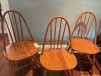 Three antique oak hoop back chairs positioned side by side showing front and angled views. Each chair has a curved hoop back with five vertical spindles and solid wood contoured seats.