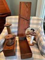 Photo of two wooden boxes, three large wooden spools (one with white thread), a large wooden mandolin slicer, and a decorative plate with a puppy image on a plaid upholstered chair.